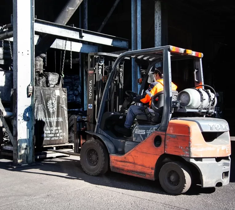 Man operating a forklift while lifting a sack of coal in a warehouse